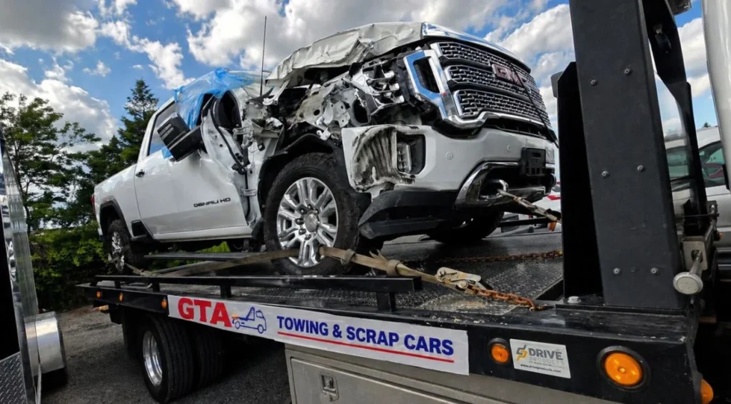 A severely damaged white GMC Denali HD truck secured on a flatbed tow truck by GTA Towing and Scrap Cars in Toronto